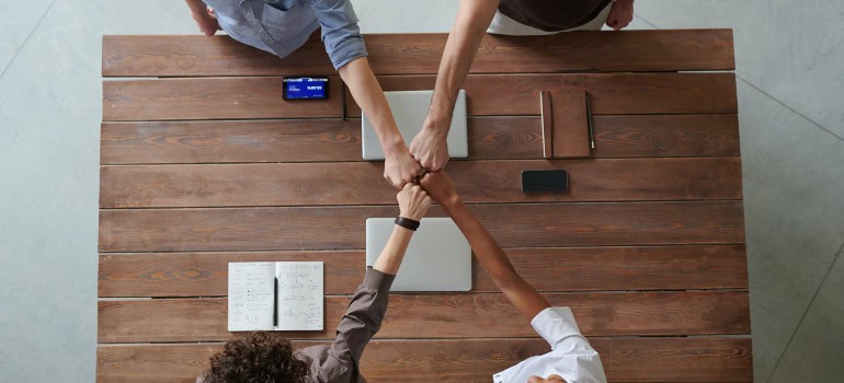 Four people are sitting at the same desk and joining fists together.