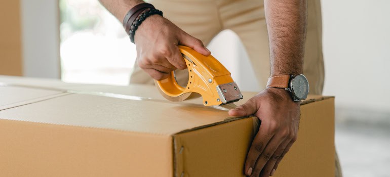 A man using duct tape to seal a cardboard box.