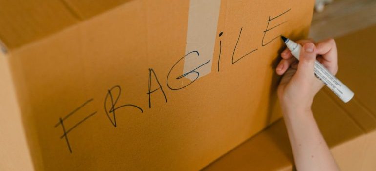 A person writting fragile on the moving box