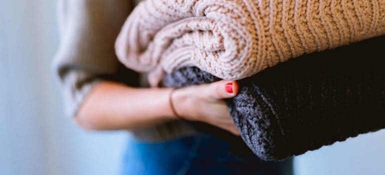 a woman packing winter sweaters for moving