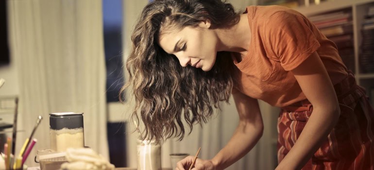 Woman in orange clothes with long hair painting in an art studio planning to settle in Lorton VA