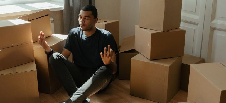 A person meditating among the boxes, thinking about how to move on a budget