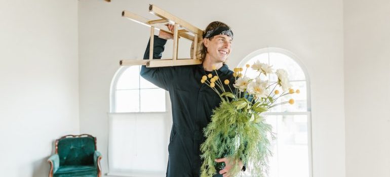 A mover with a plant and a chair in his hands