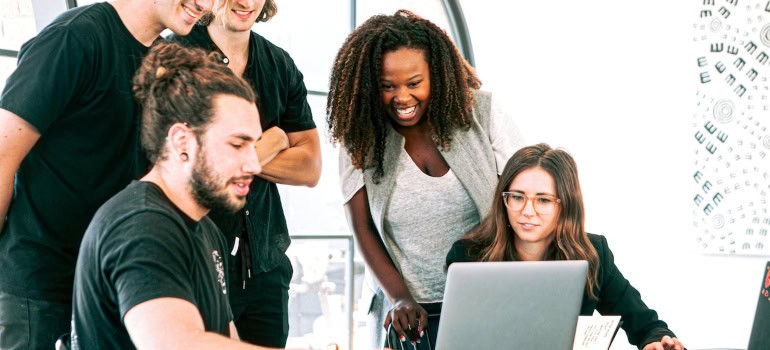 A group of people looking at a laptop screen with excitement.