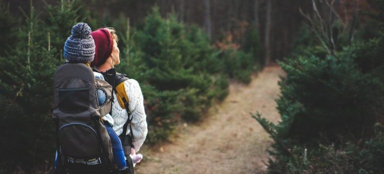 a woman walking and carrying a baby on her back while exploring places with the most beautiful nature in North Virginia