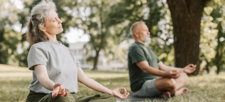 A couple of seniors doing yoga in a park.