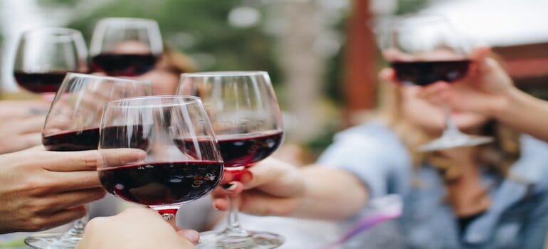 Several people toasting with glasses filled with red wine.