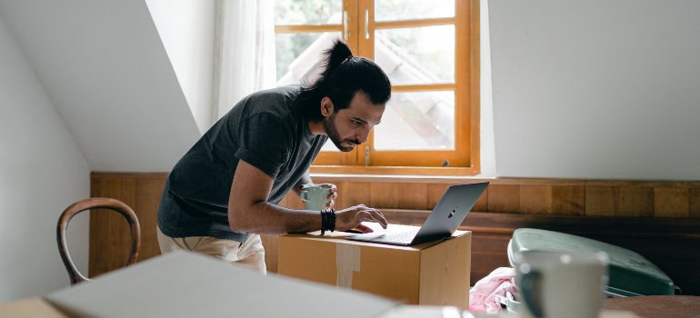 A man researching something on his laptop while surrounded by moving boxes