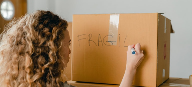 a woman writing the word "fragile" onto a moving box which is a good thing to do when protecting electronics during your move