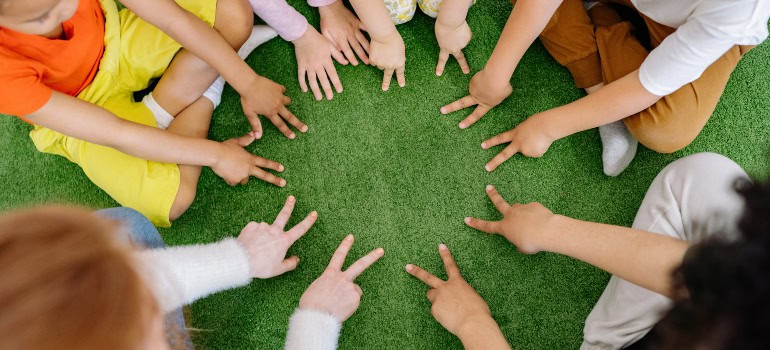 children sitting in a circle on a green rug and playing a sort of game with hands