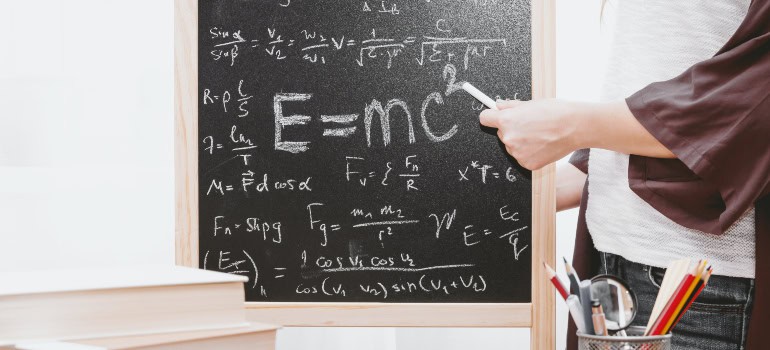 a teacher writing physics formulas on a blackboard