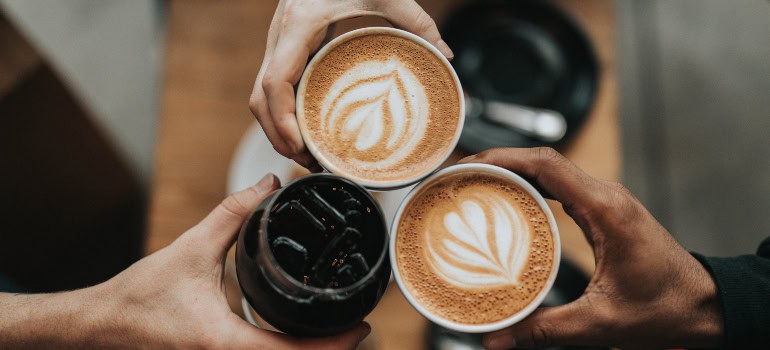 three people holding cups of coffee with interesting foam designs