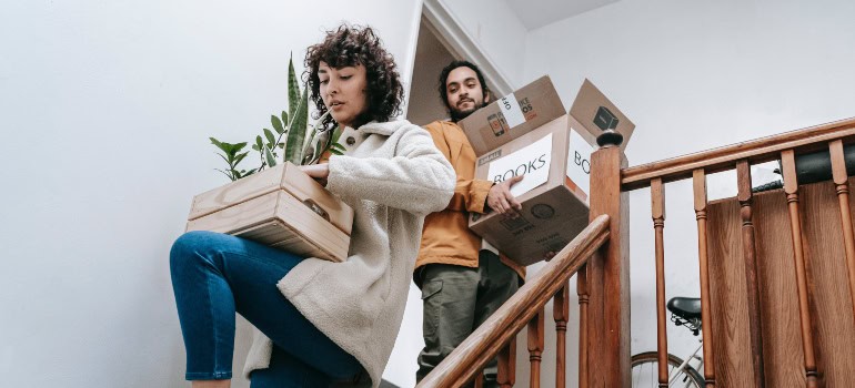 two people carrying some stuff down the stairs of which one box bears a clear label