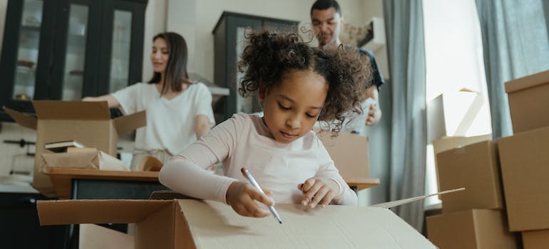 a family of three packing their kitchen items into boxes and labeling them with markers