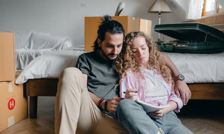 a couple creating a list together while sitting on the floor surrounded by boxes and suitcases