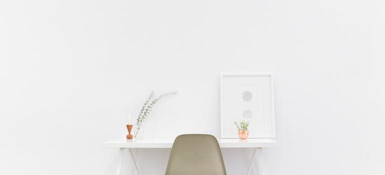 a room that is mainly empty apart from a white table, a cream chair, and a few items on the table