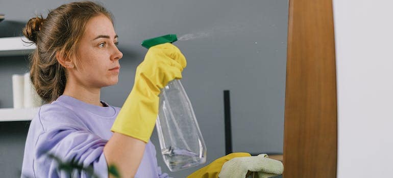 a woman holding a glass-cleaning solution in a spray while wearing yellow gloves