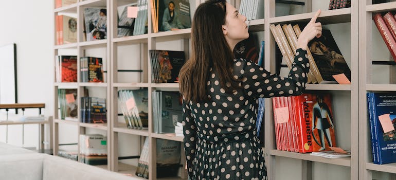 a woman sorting her books on a big, white shelf