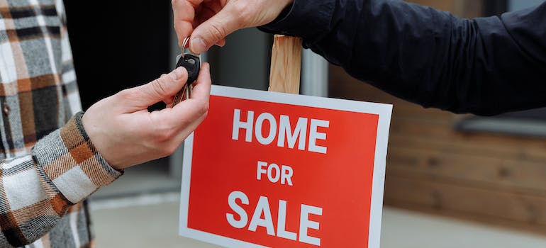 people exchanging home keys in front of the red sign that says "home for sale"