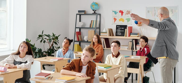 a classroom full of kids and a teacher explaining something to them