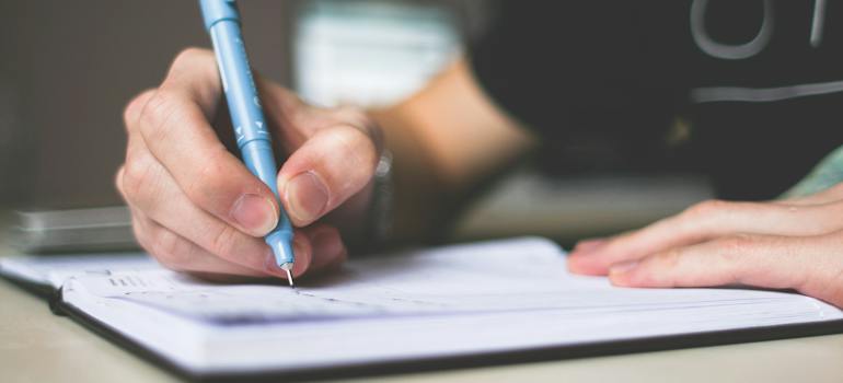 a person writing something down with a blue pen while considering things you need to watch out for when hiring a Virginia moving company