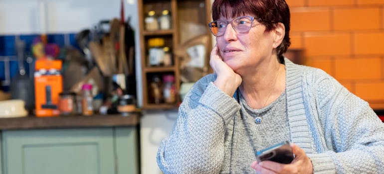 a woman thinking about something while holding a phone and sitting at a table