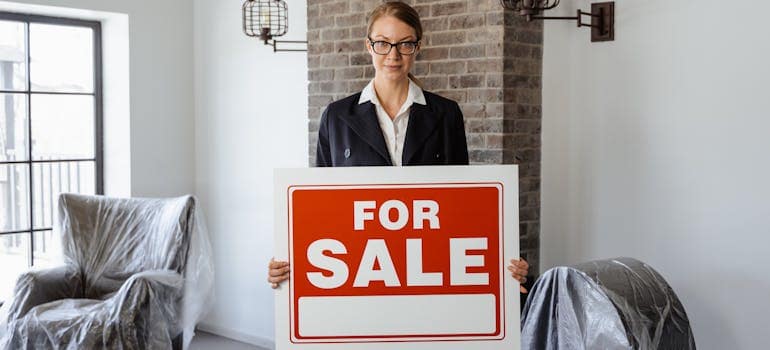 a woman standing in a home that is for sale and holding a sign that says so