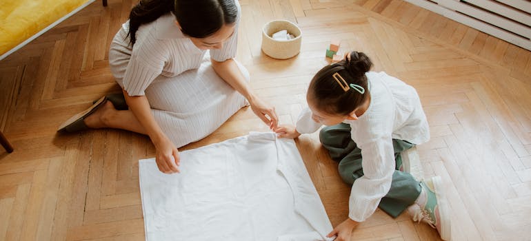 a woman and a girl are folding a white T-shirt on the floor