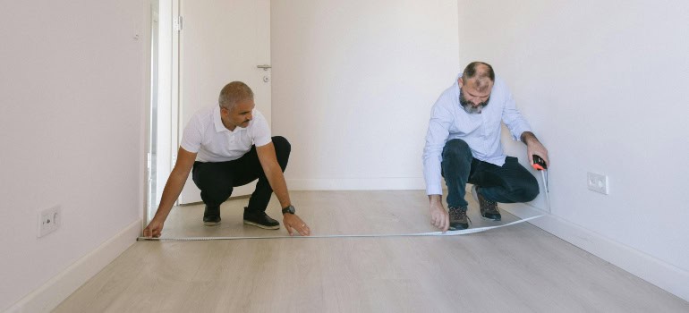 two people are measuring the floor in a room