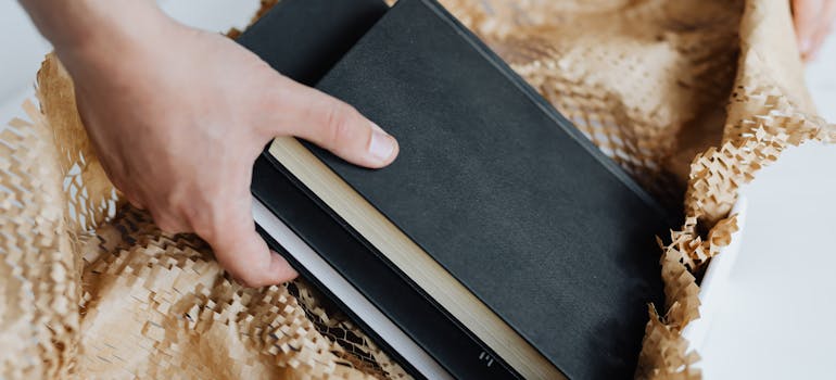 a person putting some black books and some protective material into a box