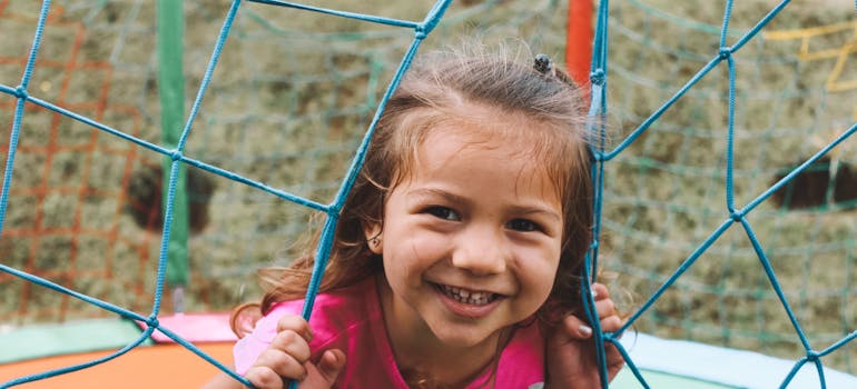 a little girl on a playground, looking through the net