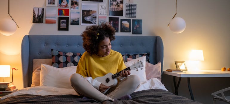 a teenage girl sitting on her bed and playing an instrument