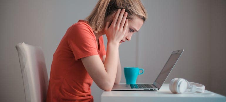 a woman working on a laptop and looking very unhappy while doing it