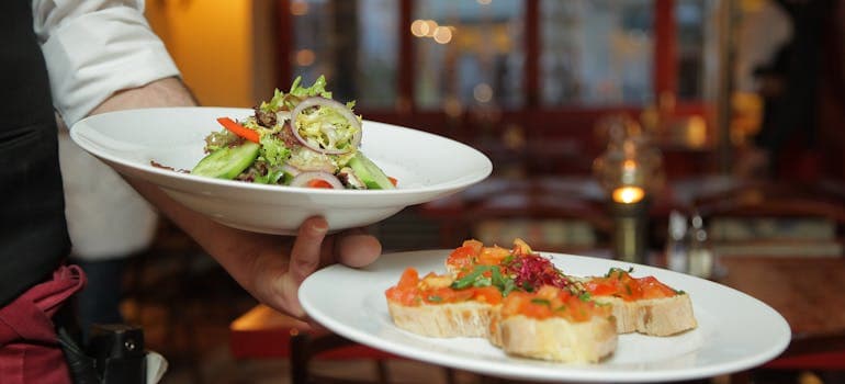 a waiter holding two plates with delicious dishes on them